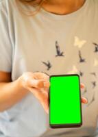 Young woman holding smartphone with green screen in her hand and showing it at camera. Soft focus. photo