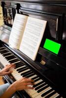 mujer manos jugando piano, sábana música y teléfono inteligente con verde pantalla a estudiando jugando piano. foto