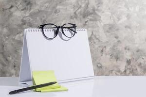 empty side of desk calendar and blank notes, glasses, pen. suitable for your schedule, gray abstract background photo