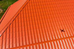 House with an orange roof made of metal, top view. Metallic profile painted corrugated on the roof. photo