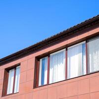 Plastic windows on the house and a spillway system on the roof. House with plastic windows and a brown roof of corrugated sheet photo