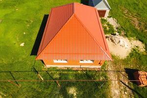 House with an orange roof made of metal, top view. Metallic profile painted corrugated on the roof. photo