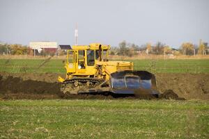 The yellow tractor with attached grederom makes ground leveling. photo