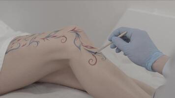 fechar acima do a artista mão desenhando temporário tatuagem em alguém perna. jovem fêmea corpo arte. pintor fazer a enfeite e decoração em dela perna video