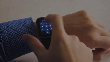 Man hand in watch with program on the screen against the background of table. Man hand at the home with watch and app on the screen. Modern smart watch with cloud of apps video