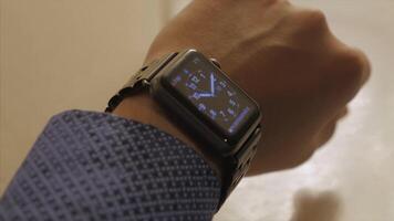 Man hand in watch with program on the screen against the background of table. Man hand at the home with watch and app on the screen. Modern smart watch with cloud of apps video