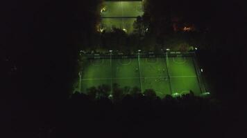 Aerial view of football pitch at night with amateur football players playing the game in the city. Clip. Football soccer field night aerial video