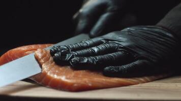 avvicinamento di Sushi capocuoco nel guanti fette fresco salmone a Sushi sbarra. affettare salmone filetti video