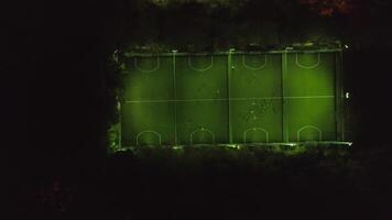 Aerial view of football pitch at night with amateur football players playing the game in the city. Clip. Football soccer field night aerial video