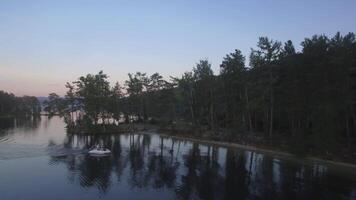 Aerial view on calm forest lake, tree forest backgrounds. Aerial view of trees on the lake shore. Forest lake landscape with reflections. The motor boat floats on the river with stone slopes and green video