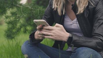 Woman sitting on the grass with a phone in her hands and a smart watch. Stock. The concept of technologies in everyday life video
