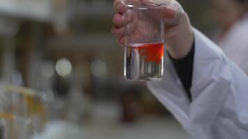 kemist händer blandad ämne av röd Färg i testa rör. läkare häller röd kemikalier in i i flaska. stänga upp video