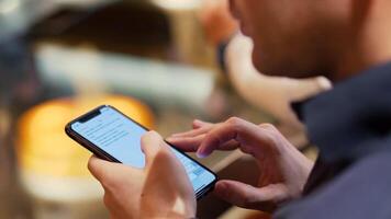 ung hipster kille textning med hans mobil telefon på de bar. stock. en ung man med en telefon i hans händer i en Kafé video