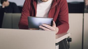 jong leerling zittend Bij bureau interactie met tablet computer en leest boeken. voorraad. onderwijs. Universiteit video