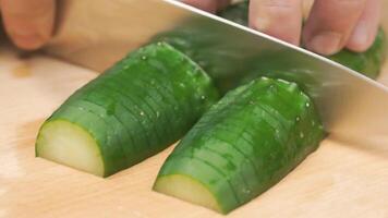 avvicinamento di mani di capocuoco affettare un' cetriolo con un' acciaio coltello su un' taglio tavola. clip. capocuoco taglio un' verde cetriolo nel il cucina video