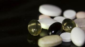 Pills spinning. Pile of several medicines. White tablets with pills on black background. Opened medicine capsule pill video