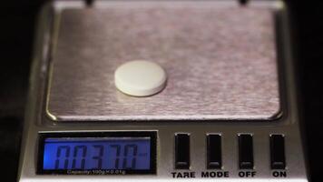 farmacéutico pone un píldora en el escamas. farmacéutico, pesa el fabricado tabletas en el controlar escamas. dieta pastillas en un escala. peso pérdida medicina derramado video