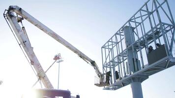 Builder on a Lift Platform at a construction site. Men at work. construction worker assembling scaffold on building site. Men assemble Billboard on tap video