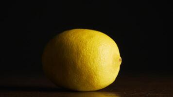 A single fresh yellow lemon on a wood grain table against a black background. Fresh lemon on the black background, closeup video