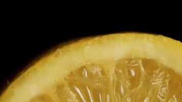 A single fresh yellow lemon on a wood grain table against a black background. Fresh sliced lemon on the black background, macro video