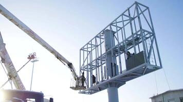 Builder on a Lift Platform at a construction site. Men at work. construction worker assembling scaffold on building site. Men assemble Billboard on tap video