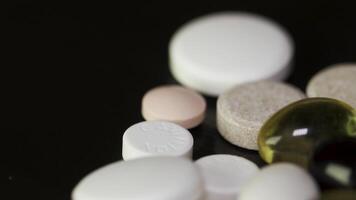 Pills spinning. Pile of several medicines. White tablets with pills on black background. Opened medicine capsule pill video