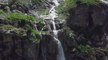 cascata fluindo baixa a partir de Alto montanhas em uma ensolarado dia. topo Visão do a montanha a partir de que a rio fluxos video