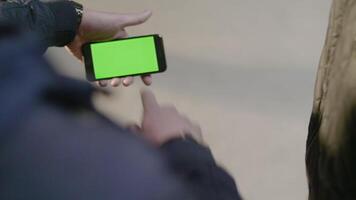 Man shows to his friend new app on his mobile phone. Phone with greenscreen. Man uses a phone with a green screen video