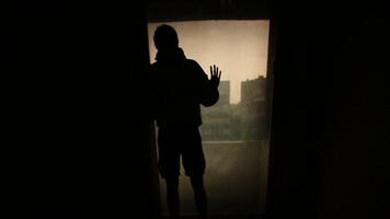 silhouette uomo guardare su il finestra con il leggero nel il camera. filmato. silhouette di un' giovane solitario uomo nel il camera. concetto di solitudine video