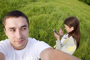 un hombre con un mujer en un prado. selfi lo hace el chico y el niña mira a el teléfono inteligente pantalla foto