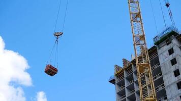 gru e edificio costruzione luogo contro blu cielo. pesante caricare sospeso su il gancio di un' gru su il costruzione di mattone sotto costruzione video