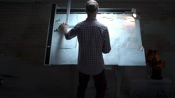 Jeune ingénieur permanent à le blanc planche avec dessin et plan retour voir. Masculin architecte permanent à dessin planche et sol plan avec crayon dans main à Bureau video