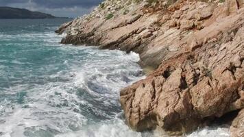 das Wellen brechen auf ein steinig Strand, Bildung ein sprühen. Filmaufnahme. planschen Wellen auf das Felsen von das Meer video