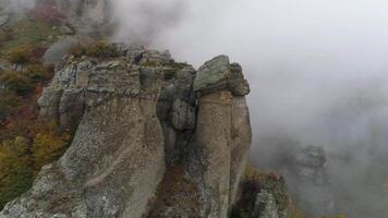 View near stone pillar of cliff. Shot. Top view of stone pillar of rock with approaching thick fog. Autumn landscape with colorful shrubs and dense gray fog on mountain video