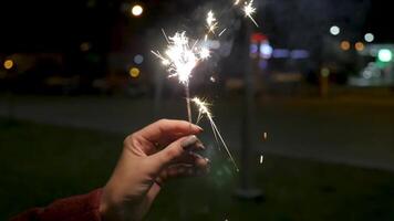 stänga upp av kvinna innehav sparkler på de gata. närbild av flicka med tomtebloss. kvinna hand innehav sparklers i de gata. Semester begrepp video