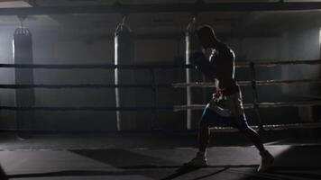 Kick box combattente ombra boxe nel il squillo. il atleta lotte con il suo ombra. giovane pugile nel formazione lancio un' punch con fasciature su il suo pugni come lui lavori su nel il squillare video