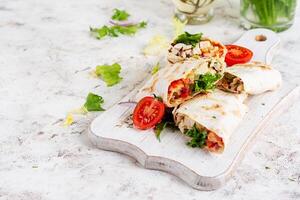 Grilled tortilla wraps with chicken and fresh vegetables on white wooden board. Chicken burrito. Mexican food. Healthy food concept. photo