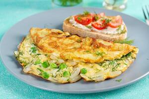 Omelette with green peas, onions and toast cream cheese, tomatoes on blue plate. Frittata - italian omelet. photo