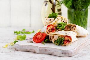 Grilled tortilla wraps with chicken and fresh vegetables on white wooden board. Chicken burrito. Mexican food. Healthy food concept. photo