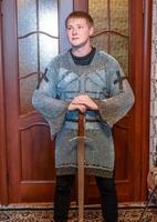 un hombre vestido arriba en un de caballero cota de malla a hogar en su habitación. de caballero espada en el manos de un hombre. foto