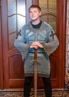 A man dressed up in a knight's hauberk at home in his room. Knight's sword in the hands of a man. photo