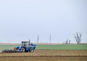 Lush and loosen the soil on the field before sowing. The tractor plows a field with a plow photo