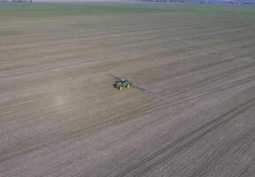 Tractor with hinged system of spraying pesticides. Fertilizing with a tractor, in the form of an aerosol, on the field of winter wheat. photo