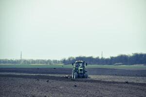 lozano y aflojar el suelo en el campo antes de siembra. el tractor arados un campo con un arado foto