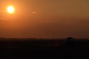 tractor arada arado el campo en un antecedentes puesta de sol. tractor silueta en puesta de sol antecedentes foto