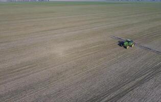 Tractor with hinged system of spraying pesticides. Fertilizing with a tractor, in the form of an aerosol, on the field of winter wheat. photo