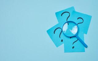 Drawn question marks on stickers and a magnifying glass, blue background. photo