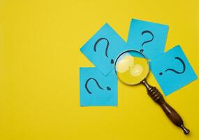 Drawn question marks on stickers and a magnifying glass, yellow background. Searching for truth and answering questions photo