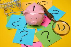 Ceramic piggy bank and stickers with drawn question marks on a yellow background, top view photo