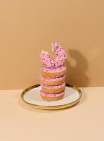 Donut covered with pink glaze and sprinkled with colorful sprinkles on a round plate photo